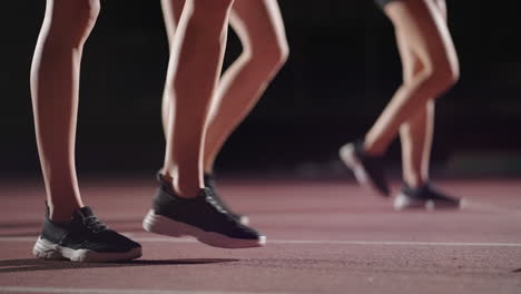 Primer-Plano-De-Las-Piernas-De-Corredoras-En-Zapatillas-De-Deporte-En-La-Oscuridad-Cerca-De-La-Línea-De-Salida,-Preparación-Y-Comienzo-De-La-Carrera